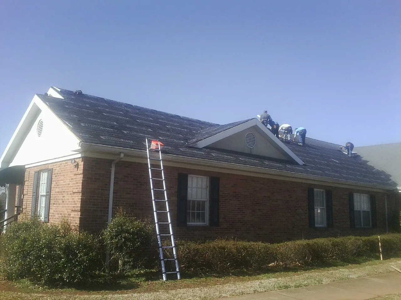 Crew tearing shingles off a brick ranch roof with a ladder set — Emergency Roof Repair work by our crew in North Dighton