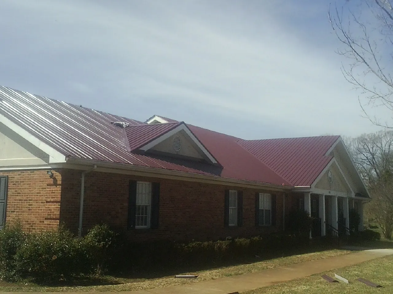 Red metal roof with gabled entries on a long brick building, from a Hail Damage Roof Repair job in North Dighton