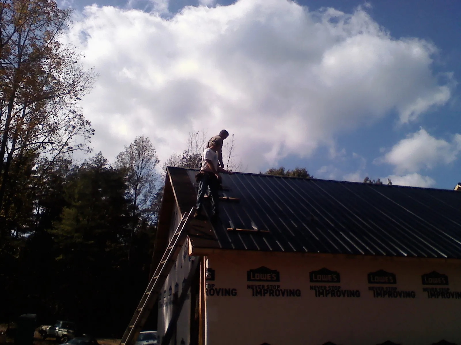 Roofer fastening dark metal panels high against a cloudy sky, from a Roof Inspection job in North Dighton