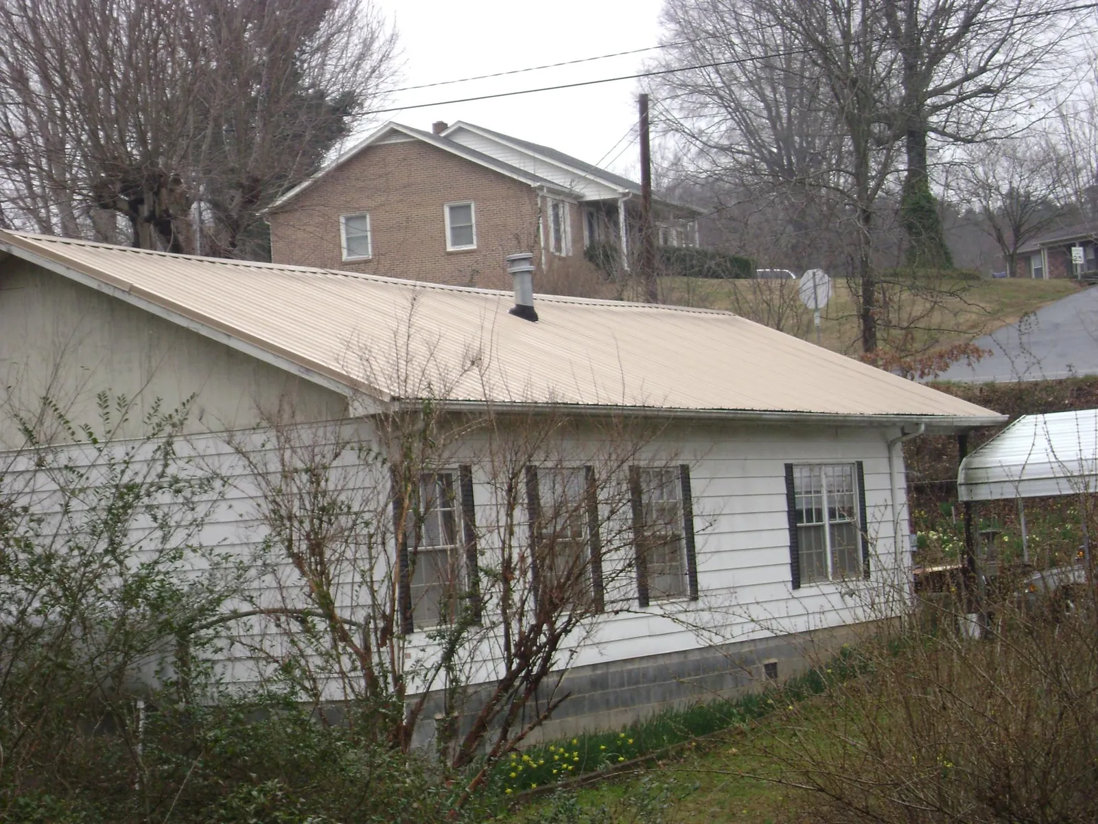 Tan metal roof on a white sided house set into a hillside — Commercial Roofing by Roofing Brothers in North Dighton