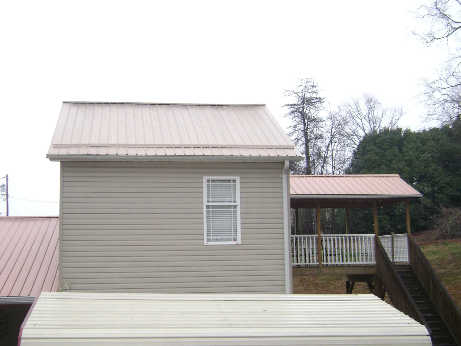 Tan metal roofs on a two story addition and attached porch, from a Roof Replacement job in North Dighton